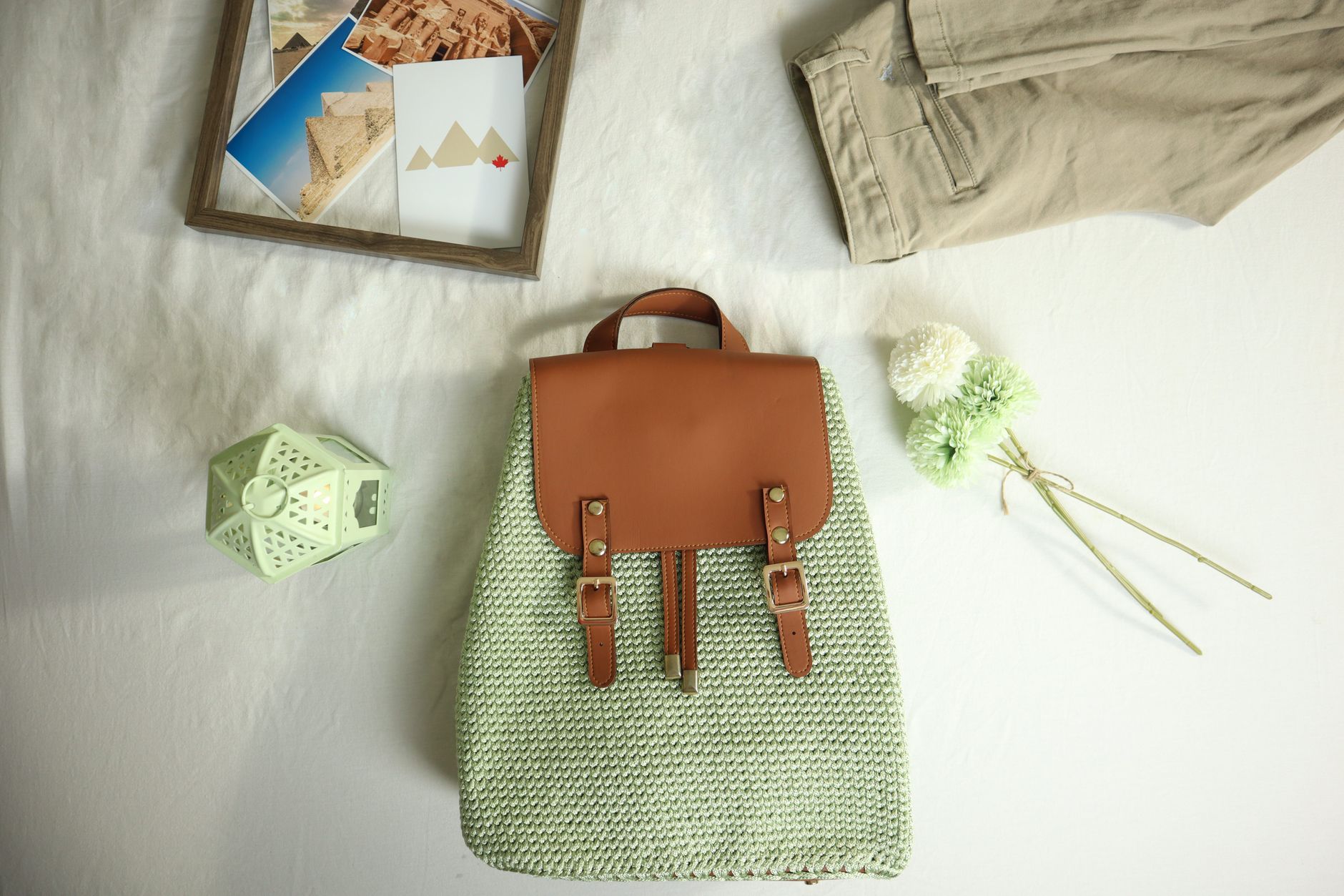 A handcrafted crochet backpack with leather accents alongside travel-themed items in a flat lay composition.
