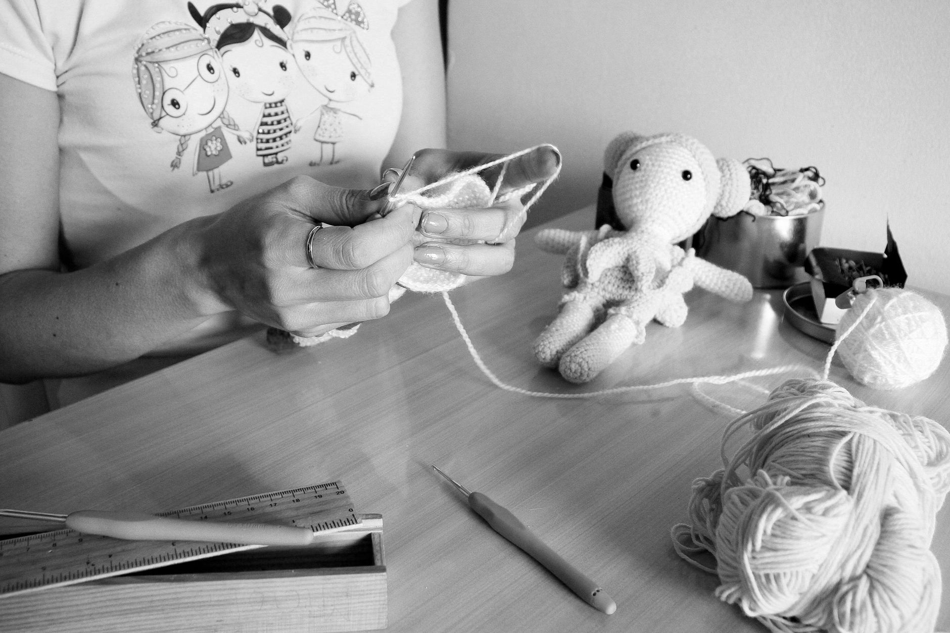 Woman knitting indoors with yarn and crochet tools, featuring a handmade soft toy.