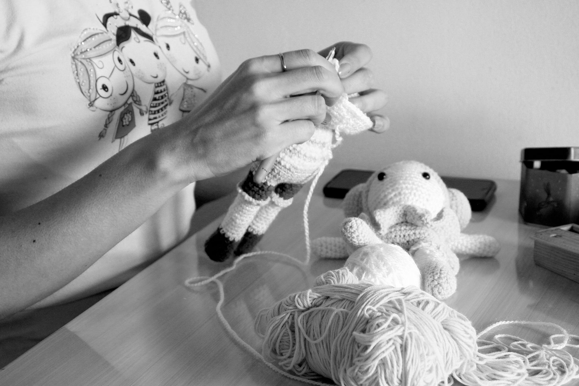 Person knitting ragdoll with yarn and crochet tools, black and white image.