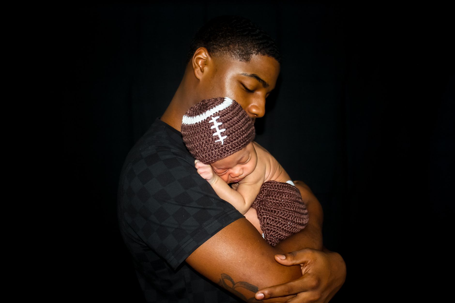 Intimate portrait of a father lovingly holding his sleeping baby against a black background.