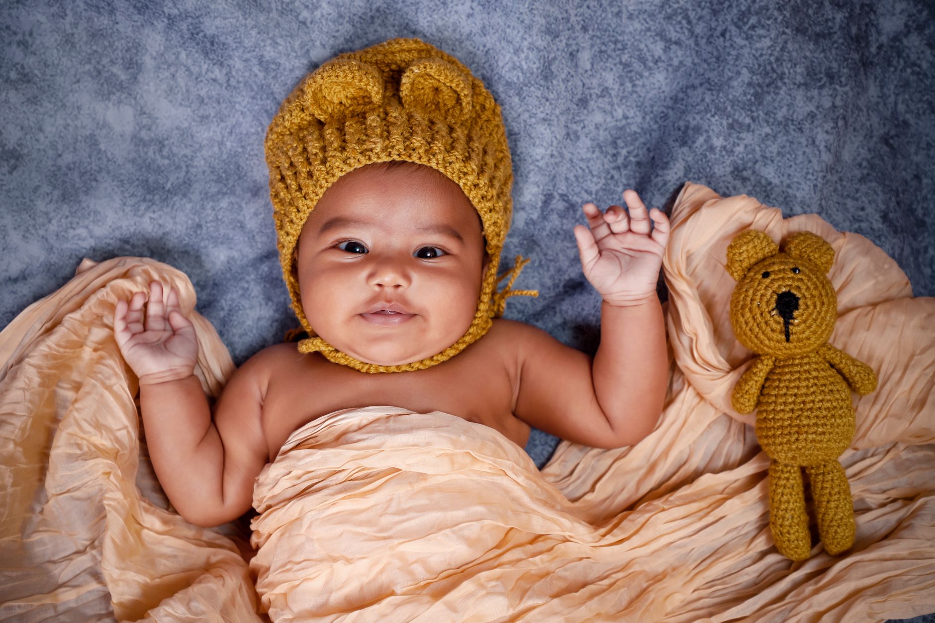 Charming newborn baby with a knitted cap lying on a blanket beside a crochet teddy bear.