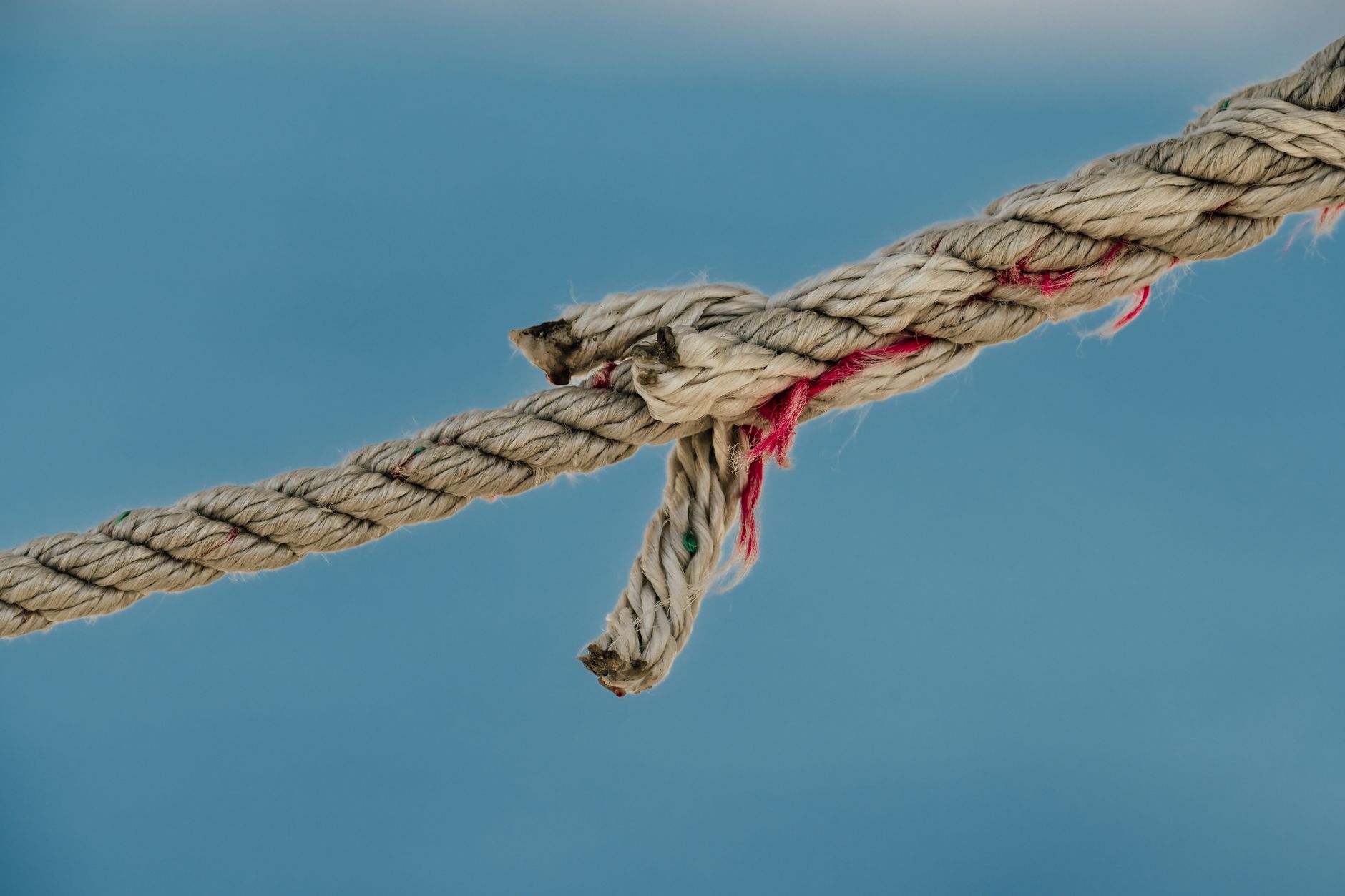 A detailed close-up photograph of a frayed nautical jute rope against a soft blue background.