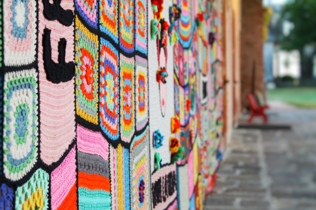 Vibrant crochet artwork displayed on a brick wall in an outdoor setting, showcasing handmade artistry.