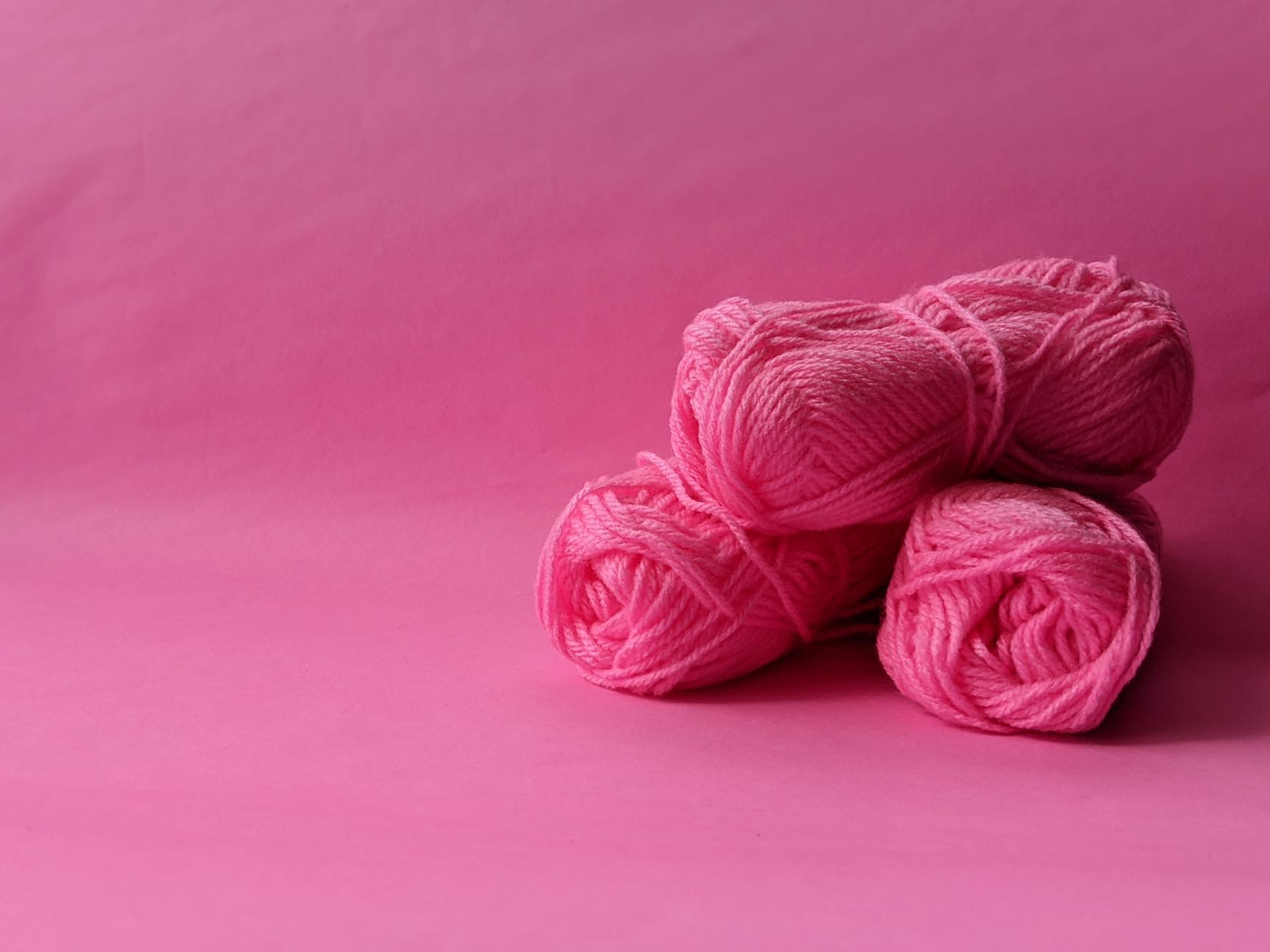 Three pink yarn balls on a monochrome pink background, perfect for knitting and crafts.