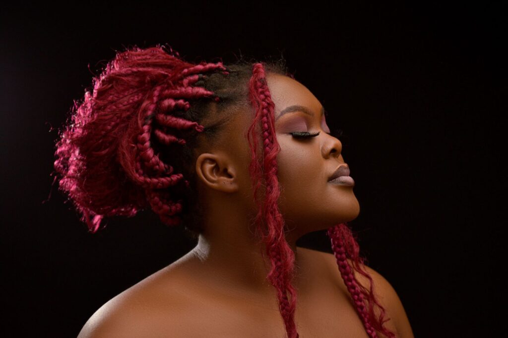 Artistic portrait of a woman with pink braided hair on a black background.