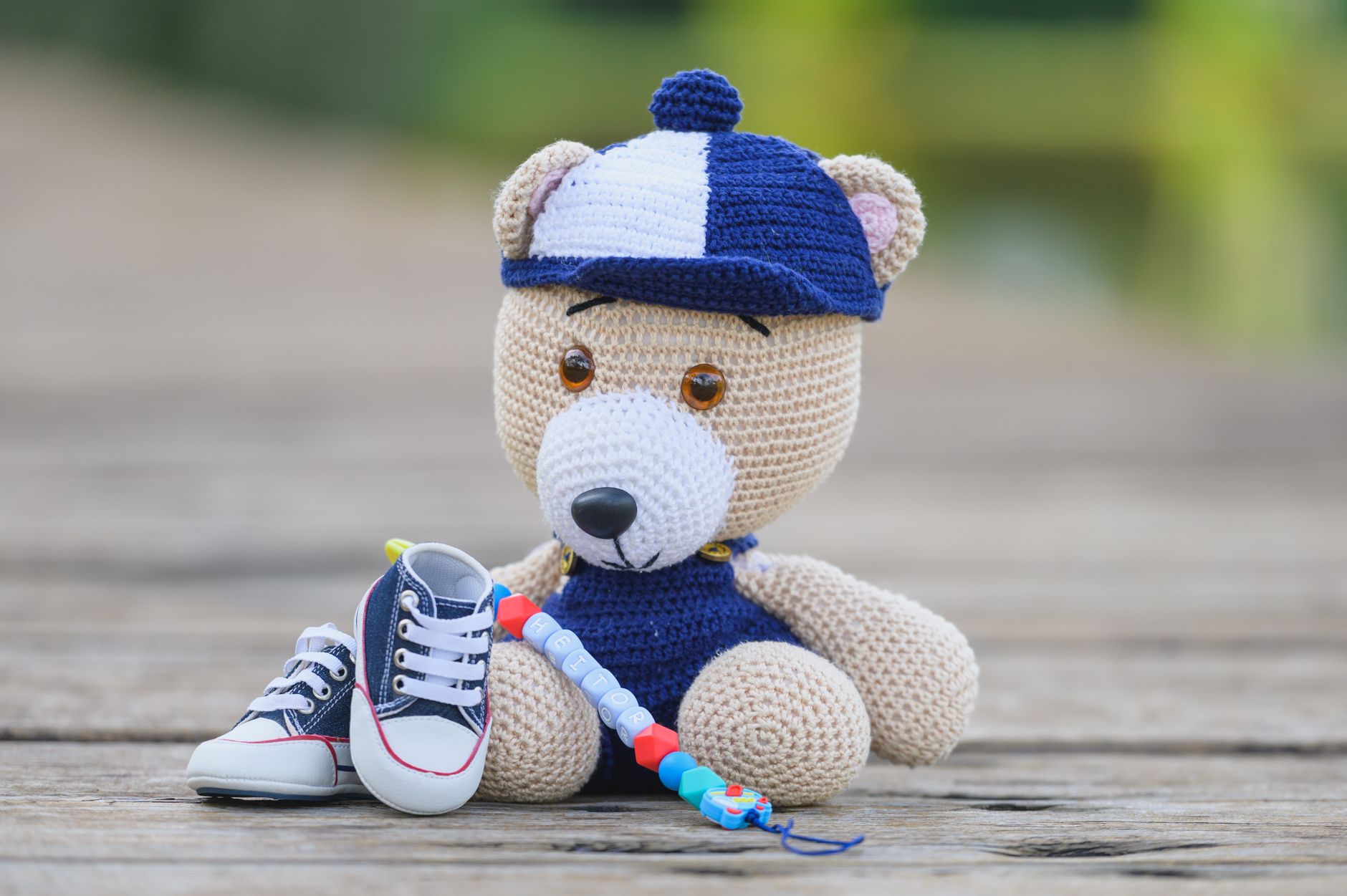 Cute crocheted teddy bear with baby shoes and beaded toy on a wooden background.