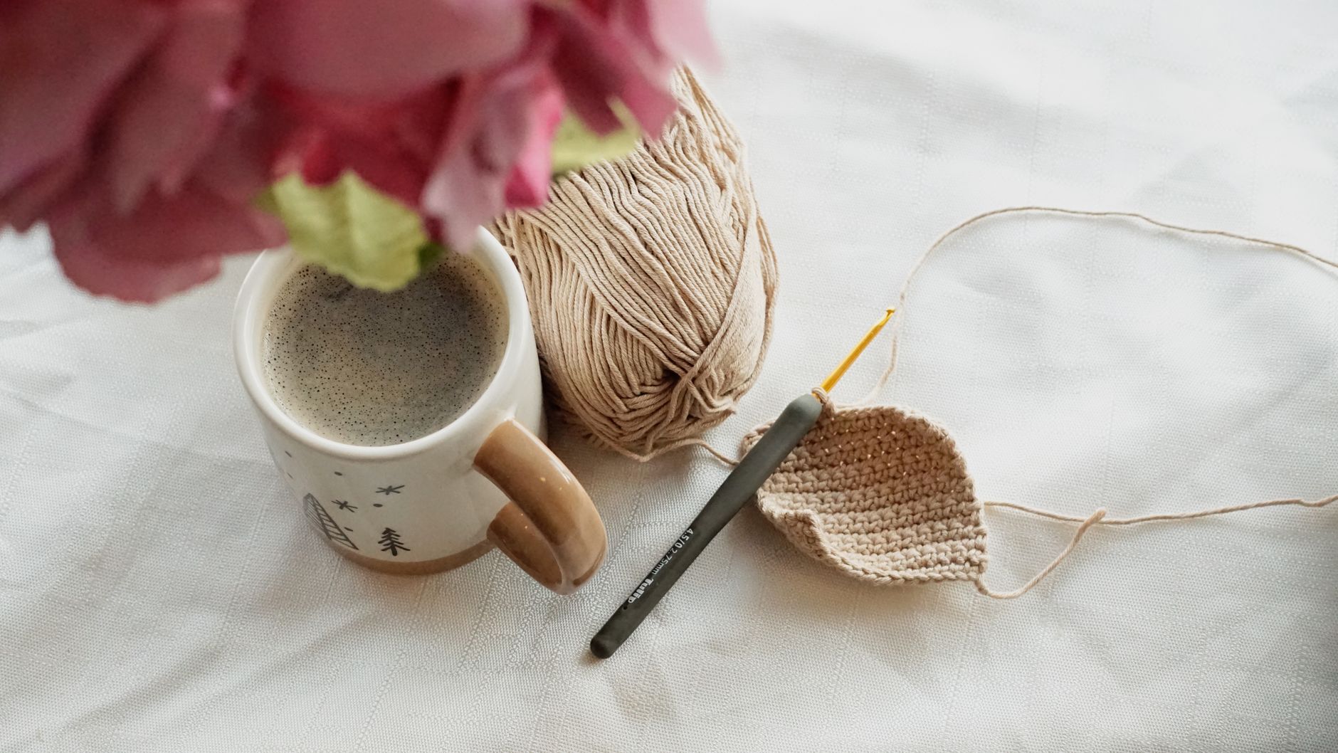 Relaxing scene with coffee, crochet project, and yarn on a table.