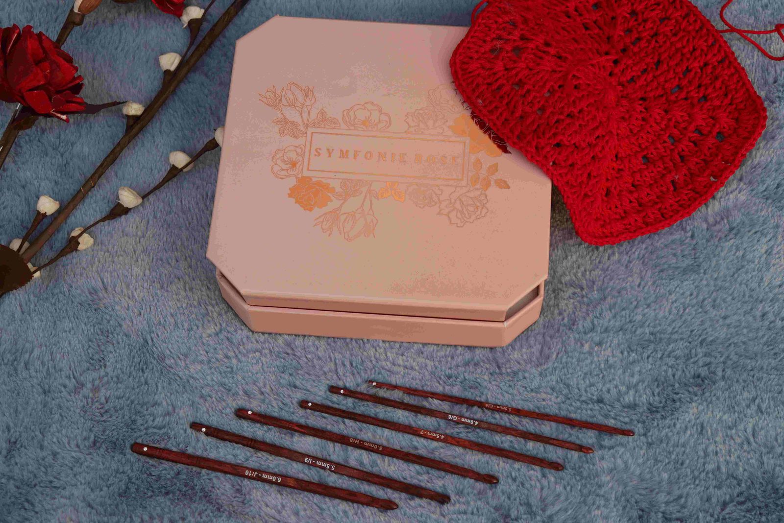 Flat lay of crochet set with hooks, red doily, and decorative box on fabric.