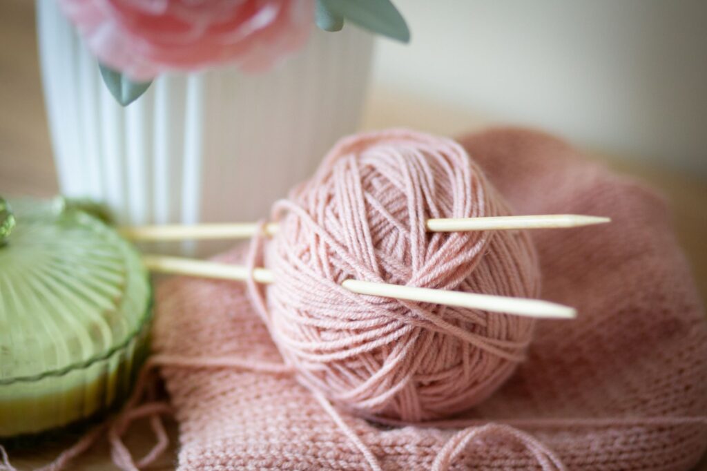 Close-up of pastel pink yarn and knitting needles. Ideal for handmade crafts and needlework themes.