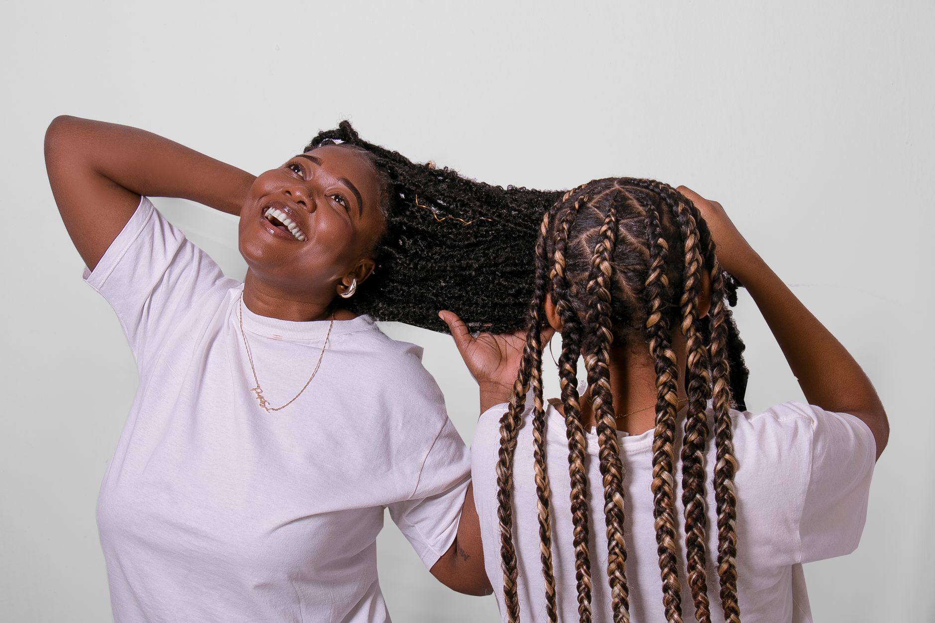 Two women with braided hairstyles enjoying a fun, casual moment indoors.