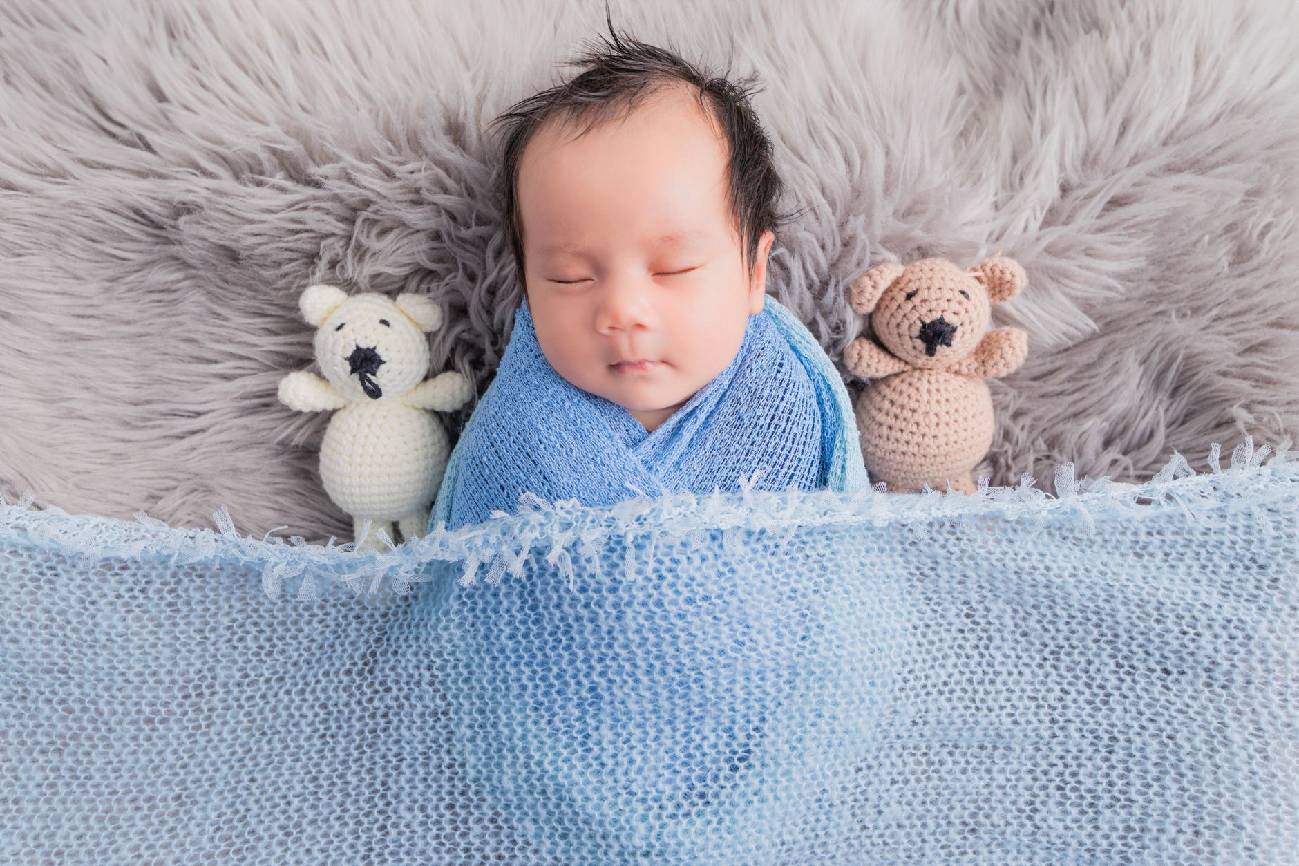 Cute baby wrapped in blue blanket peacefully sleeping with plush toys.