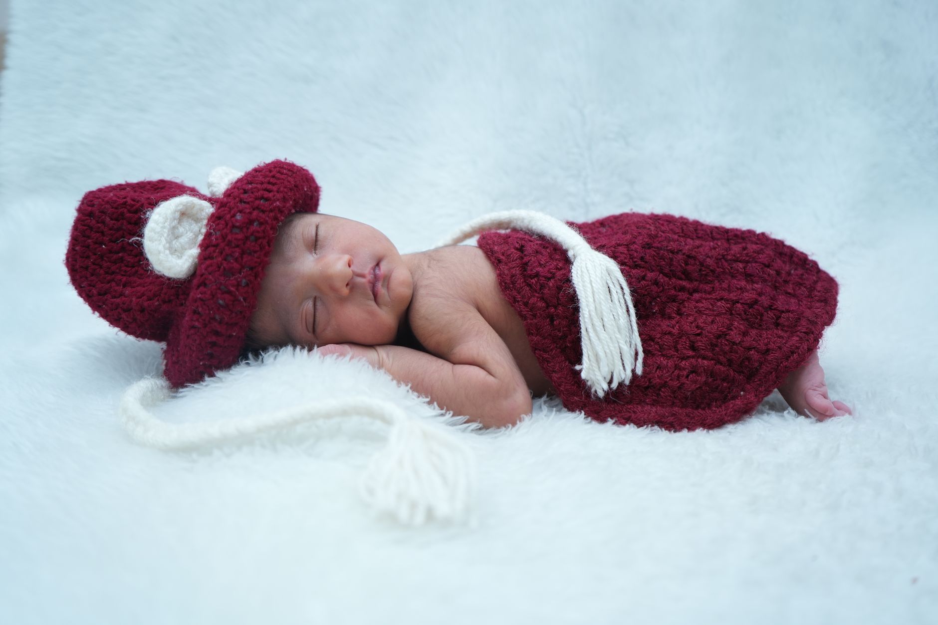 Charming newborn baby peacefully sleeping in a cozy red knitted outfit on a soft white surface.