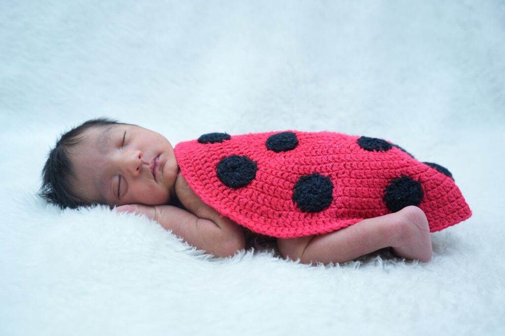 A peaceful newborn baby sleeps on white fur, dressed in a cute ladybug costume.