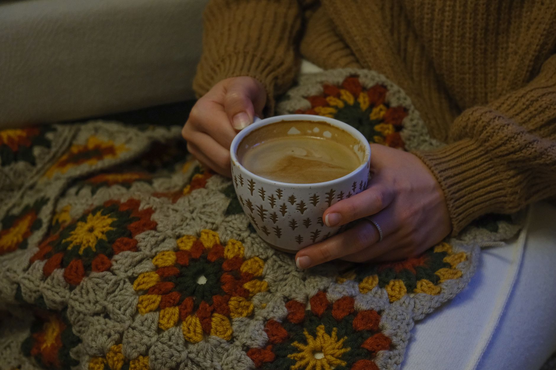 A person holding a warm coffee cup wrapped in a handmade crochet blanket, creating a cozy autumn vibe.