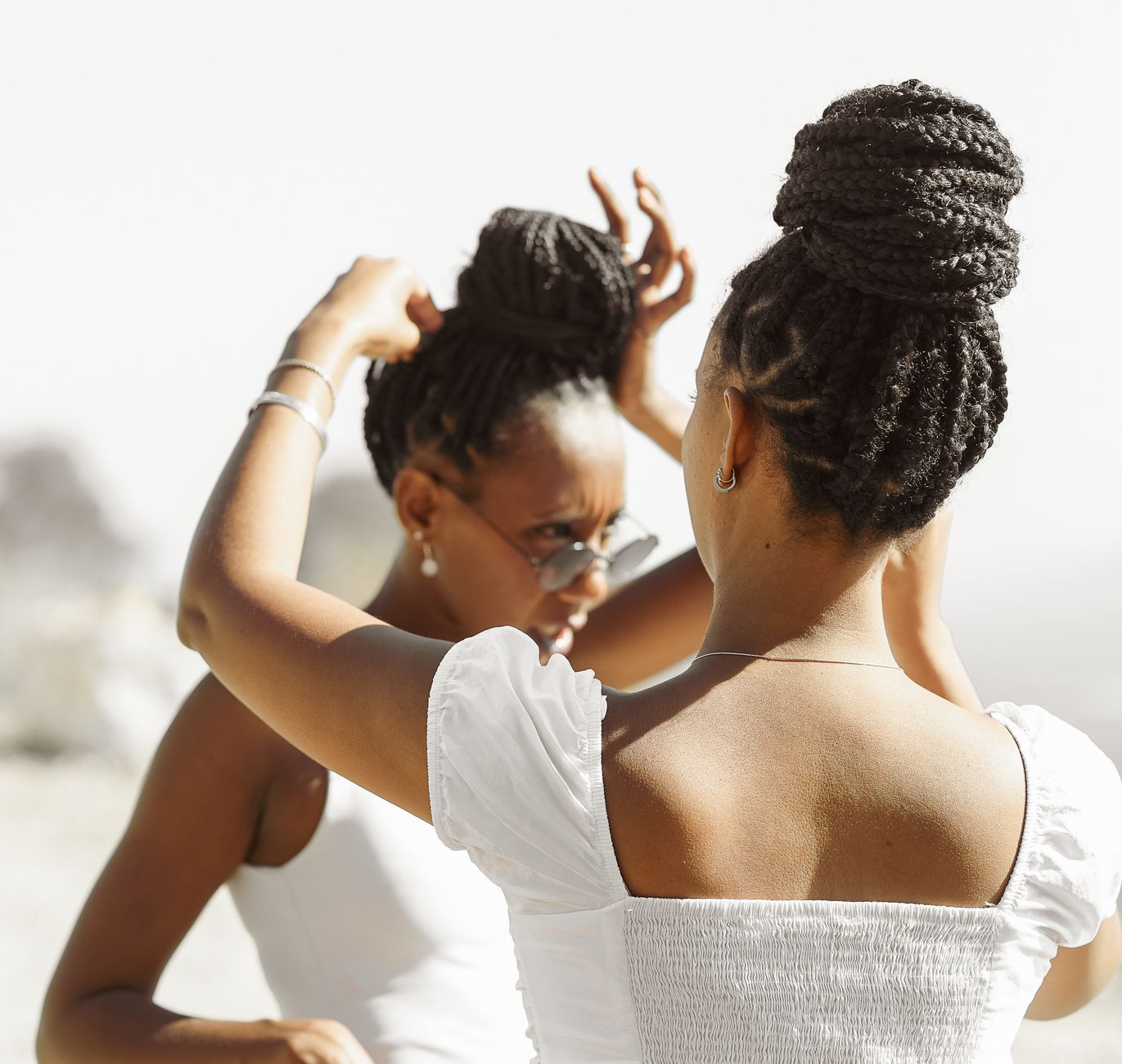 Two women styling hair outdoors, showcasing friendship and elegance on a sunny day.