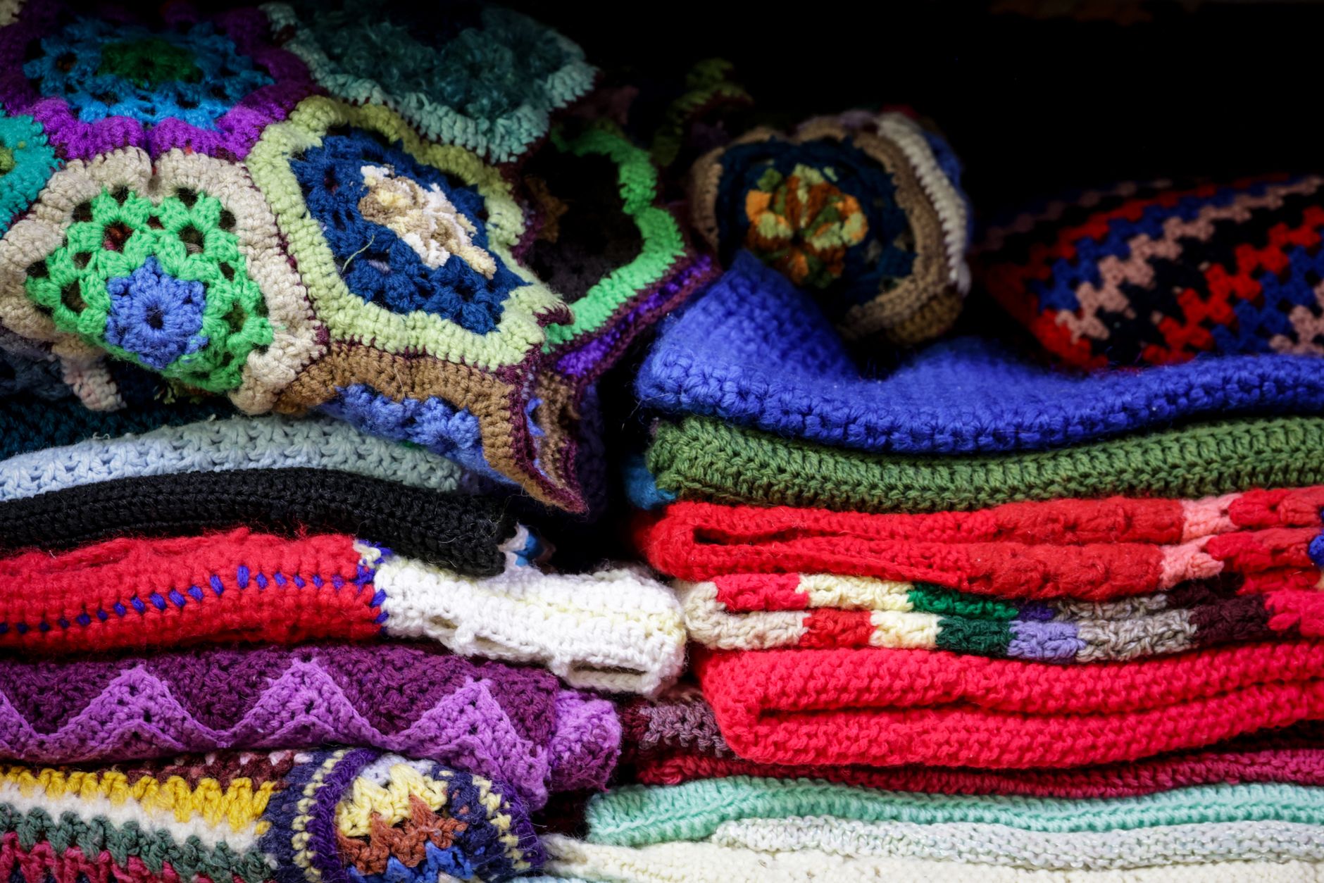 A vibrant stack of vintage crochet blankets showcasing intricate patterns and colorful designs.