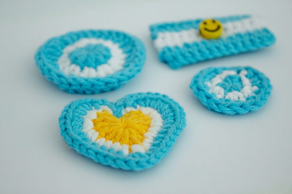 Colorful crocheted items inspired by the Argentine flag, featuring blue and white colors with a yellow heart.