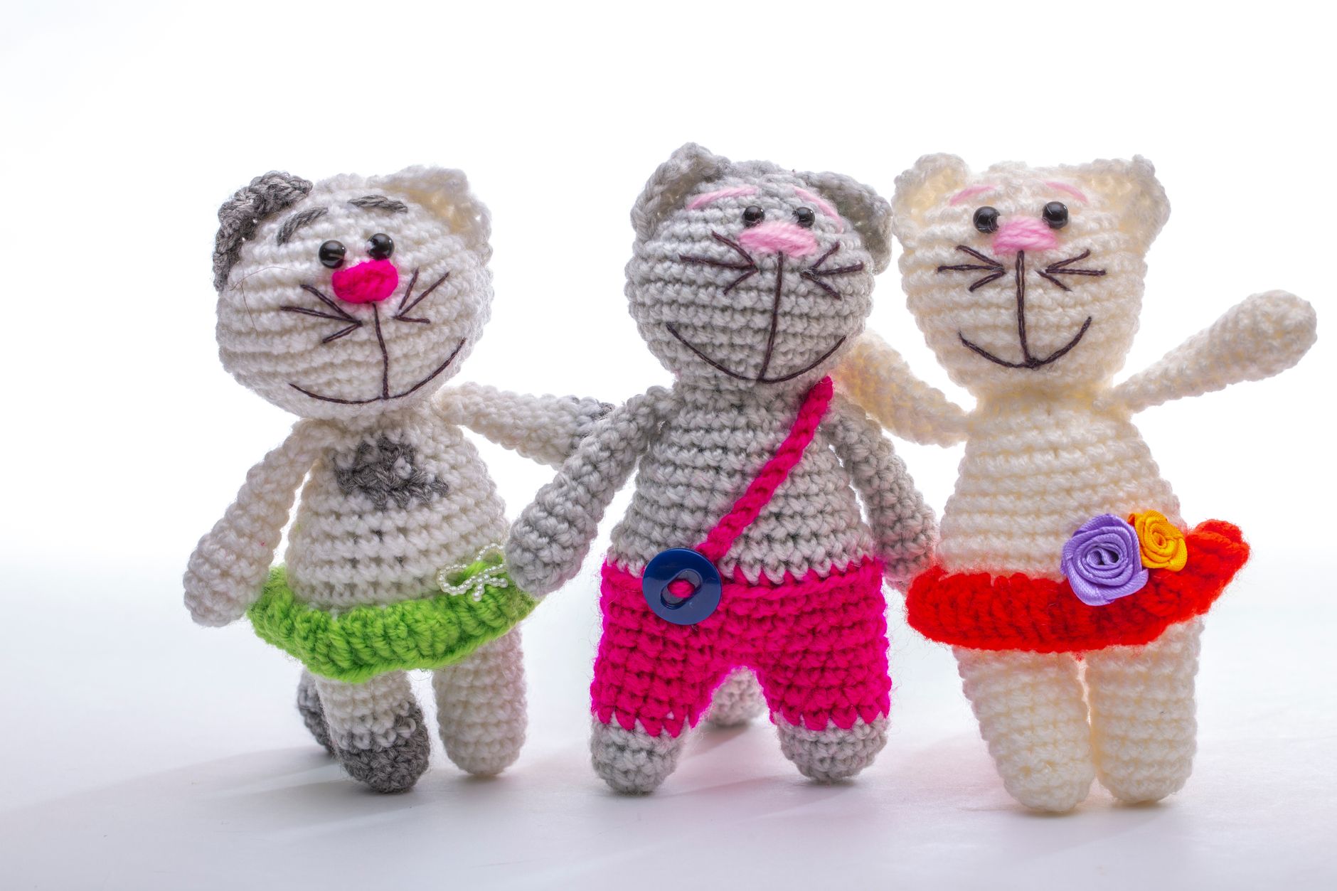 Three colorful crocheted cat dolls with unique outfits against a white background, showcasing craft artistry.