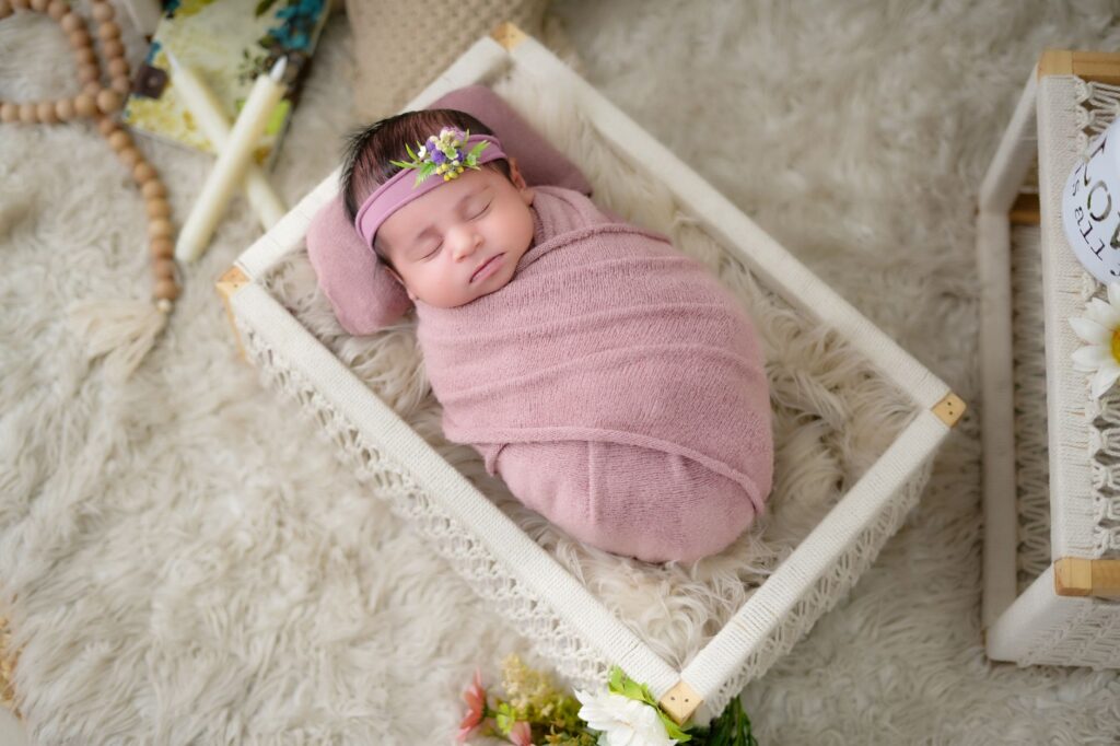 Peaceful newborn baby wrapped in a pink blanket, sleeping in cozy wicker basket with floral decor.