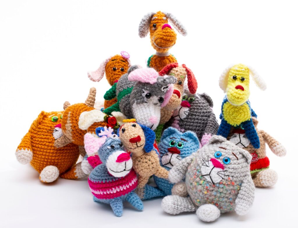 A group of vibrant, hand-knitted animal toys arranged together against a white background.