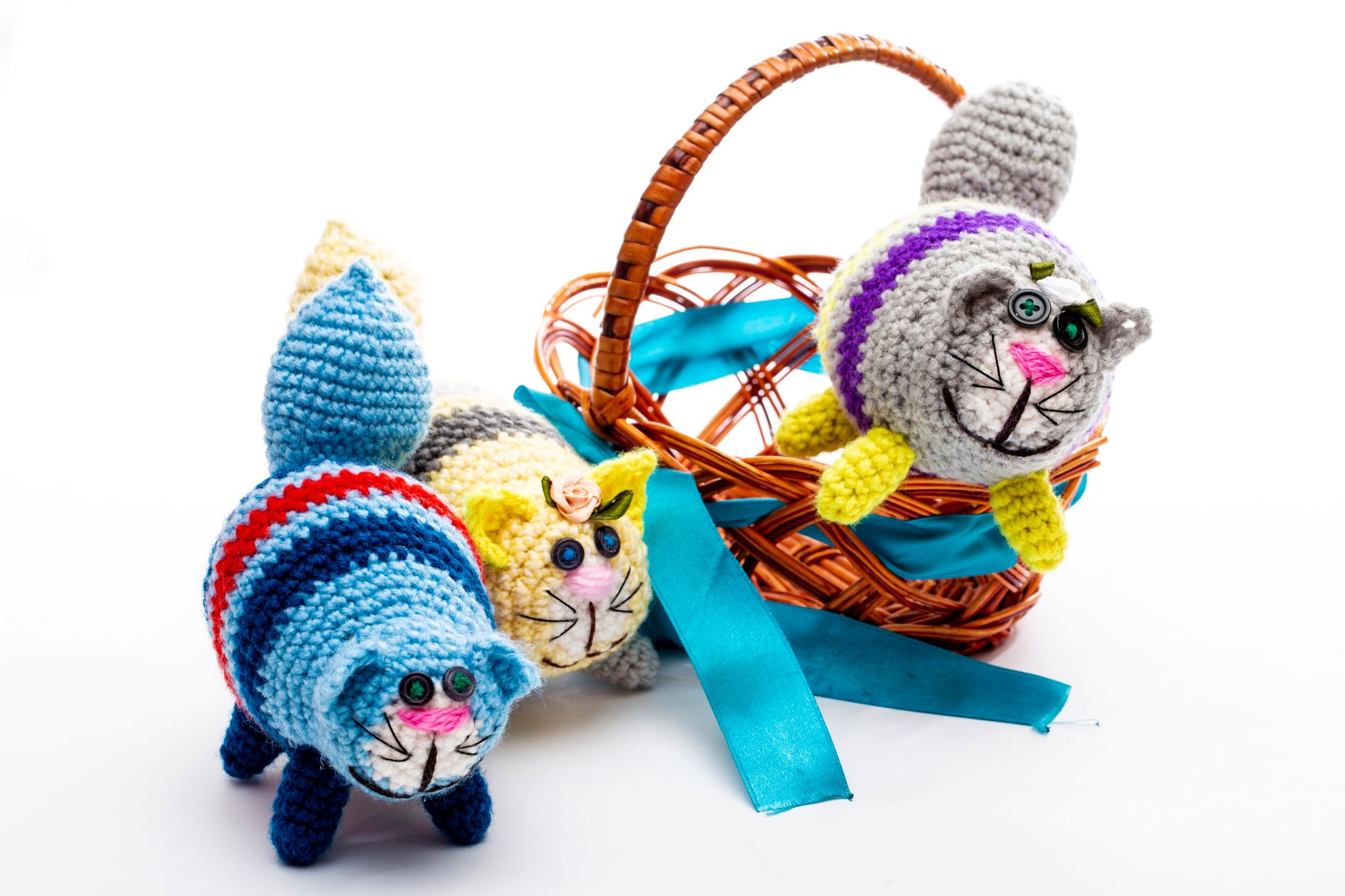 Three vibrant crochet cat toys in a wicker basket with blue ribbon on a white background.