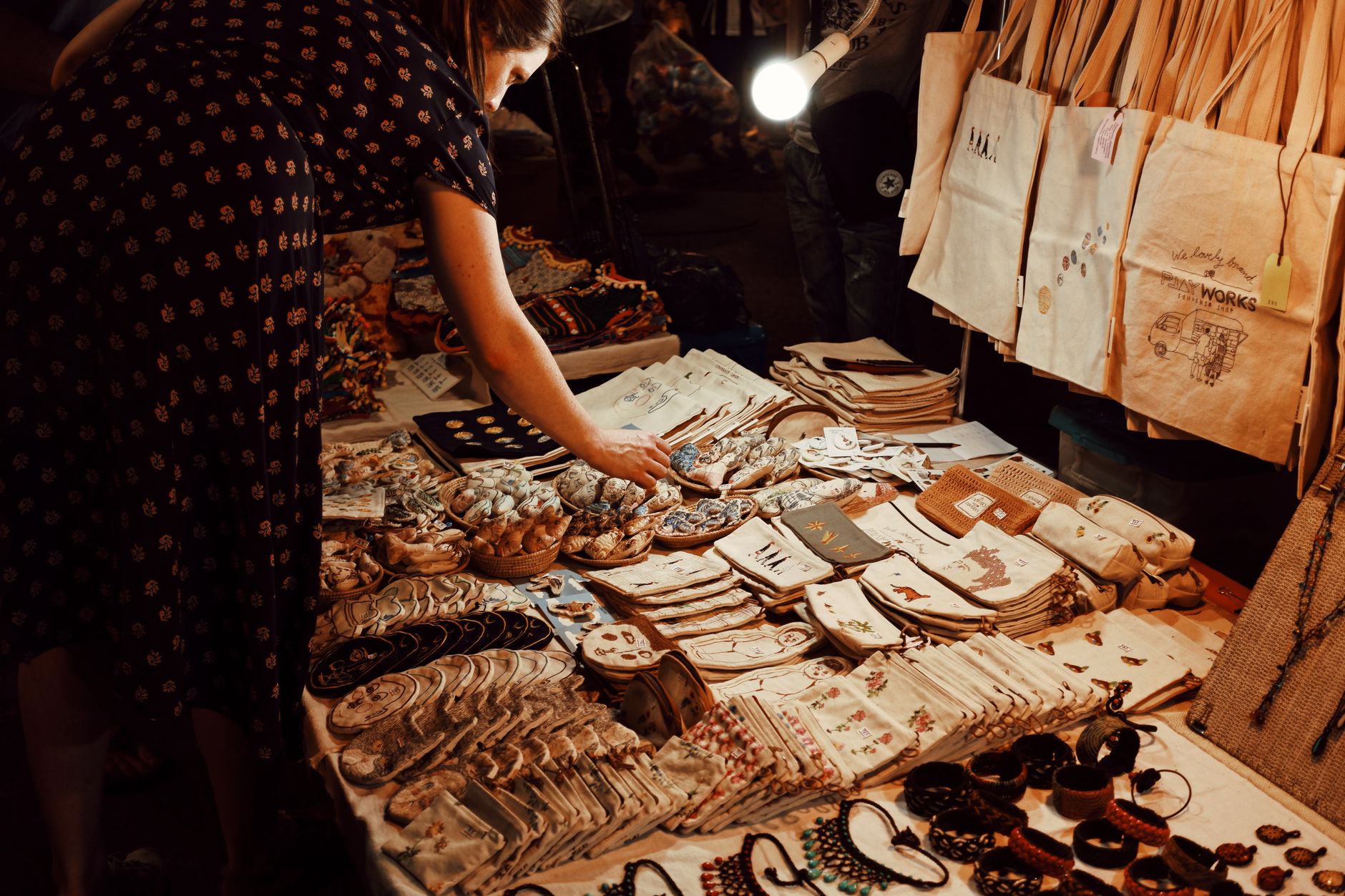 From above crop female customer in dress choosing handmade goods from table in local souvenir bazaar in evening