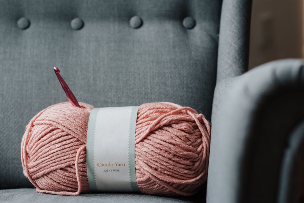 Soft pink yarn for knitting with crochet hook on gray cozy couch at home