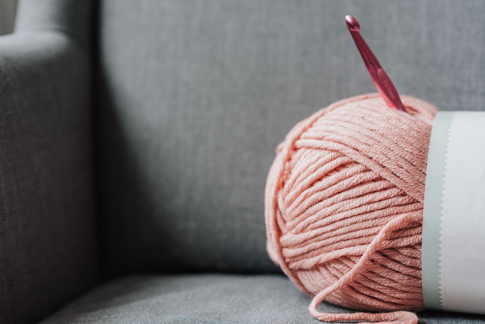 Soft pink yarn for knitting with metal crochet hook on cozy gray couch at home