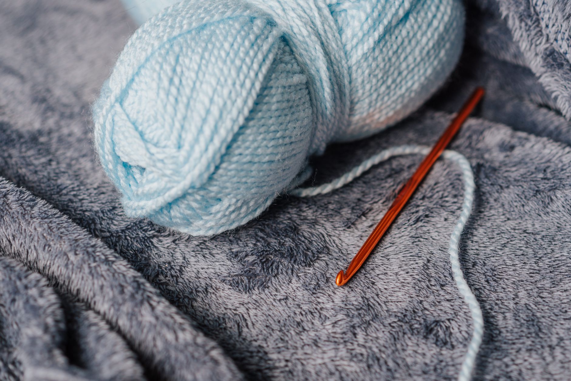 High angle of soft blue yarn for knitting near crochet hook on couch at home