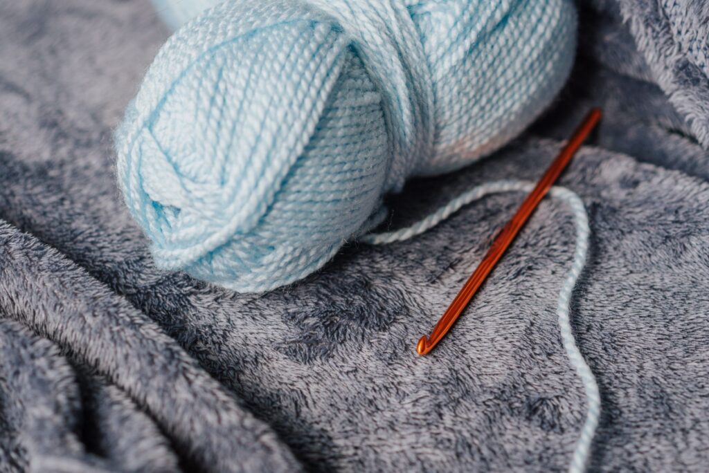 High angle of soft blue yarn for knitting near crochet hook on couch at home
