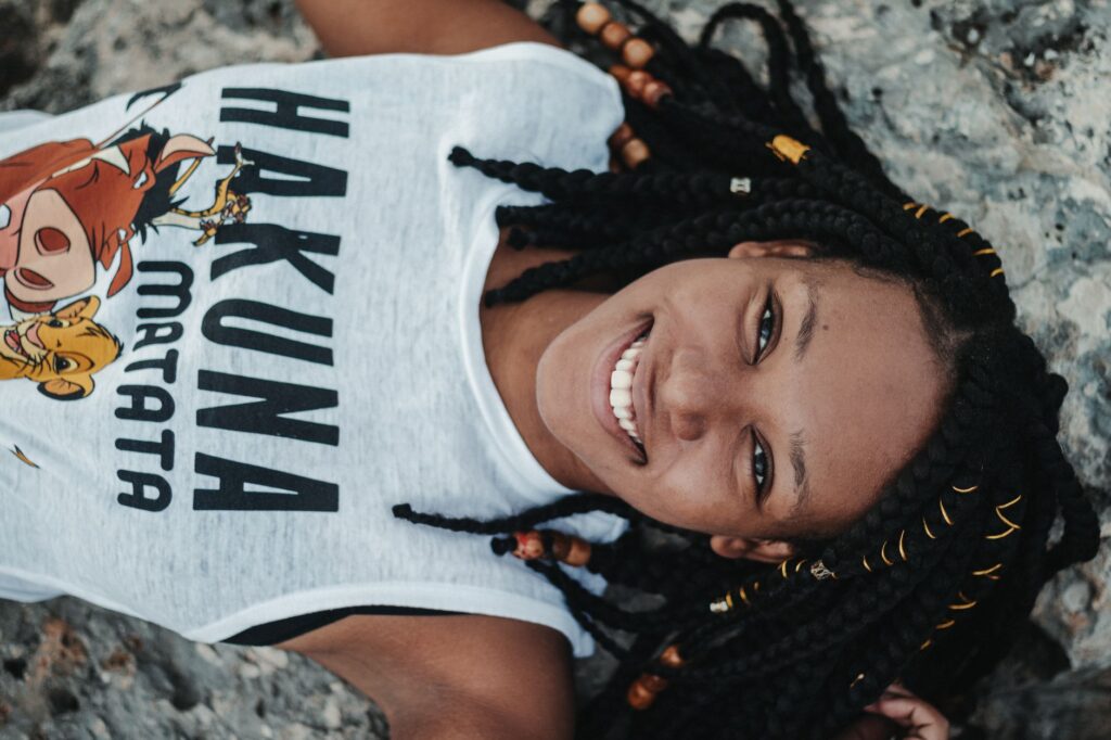 Top view of young cheerful black female in stylish clothes with inscription and image looking at camera while lying on stone