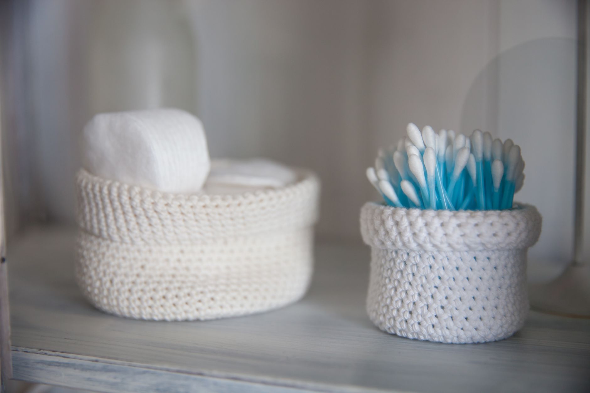 A close-up of cotton swabs and pads in crocheted baskets, creating a soft, neutral, and cozy bathroom atmosphere.