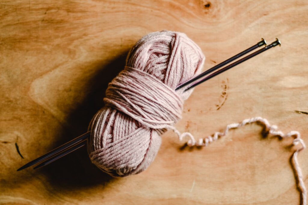 A ball of pink yarn with knitting needles resting on a wooden table, perfect for craft enthusiasts.