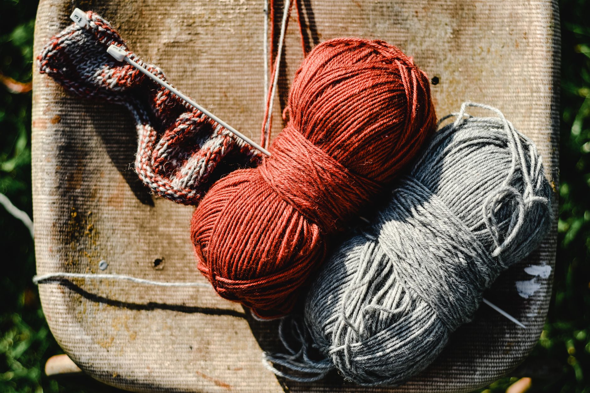 Warm yarn balls in red and grey with knitting needles on a rustic chair, crafting close-up.