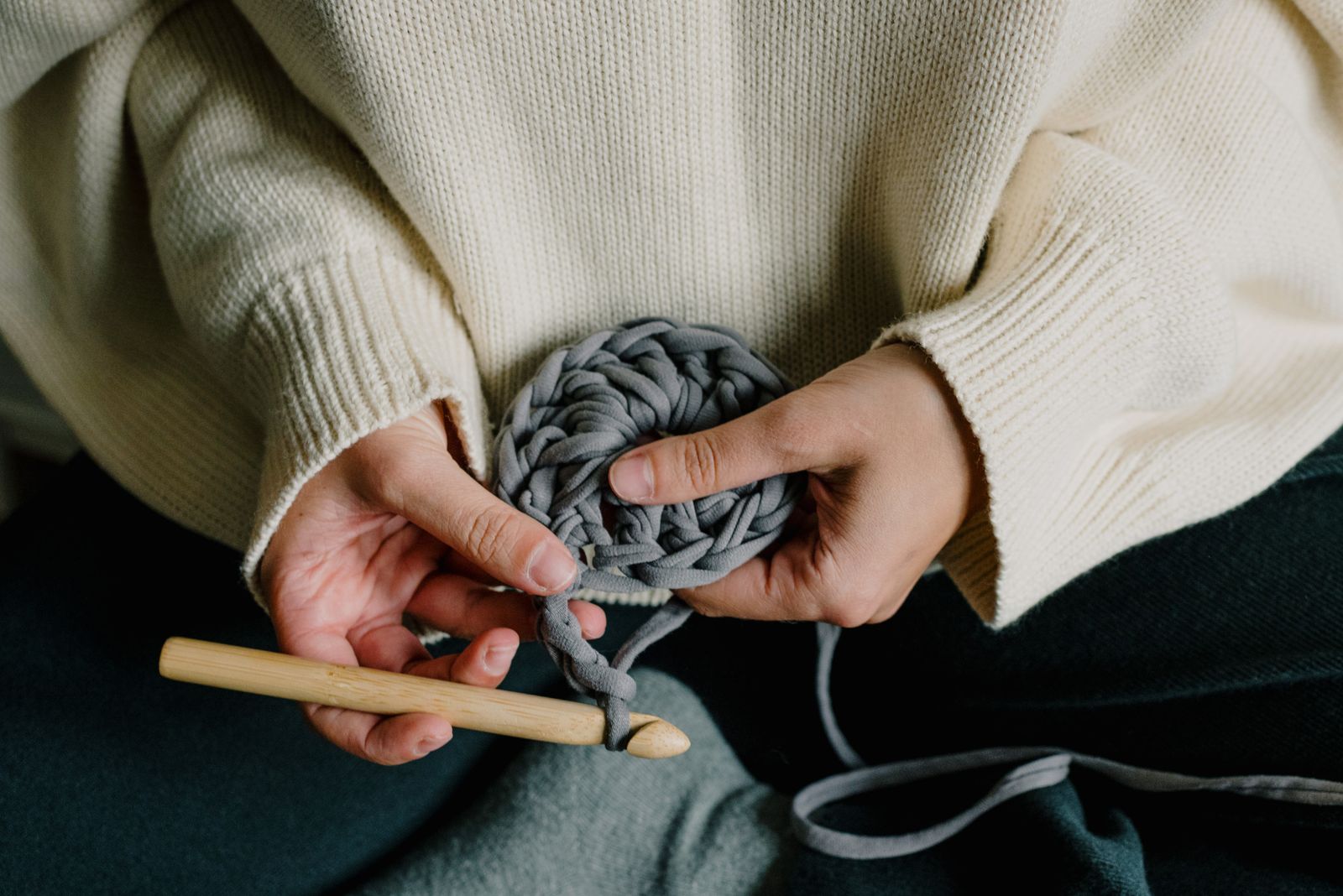 Detailed close-up of hands using a crochet hook with grey yarn, showcasing the art of crochet.