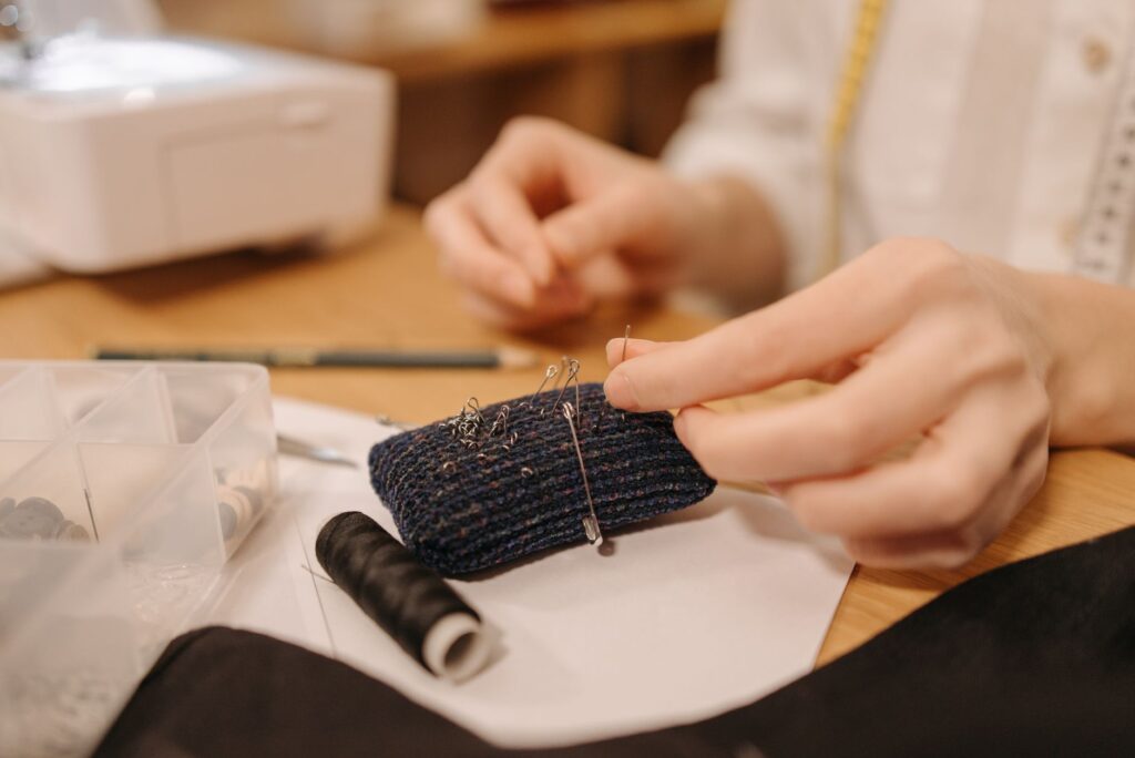 Hands working on sewing fabric with pins and needles, close-up view.