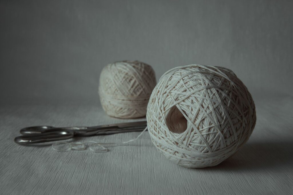 Close-up image of white yarn balls and scissors on a plain table, showcasing minimalism.