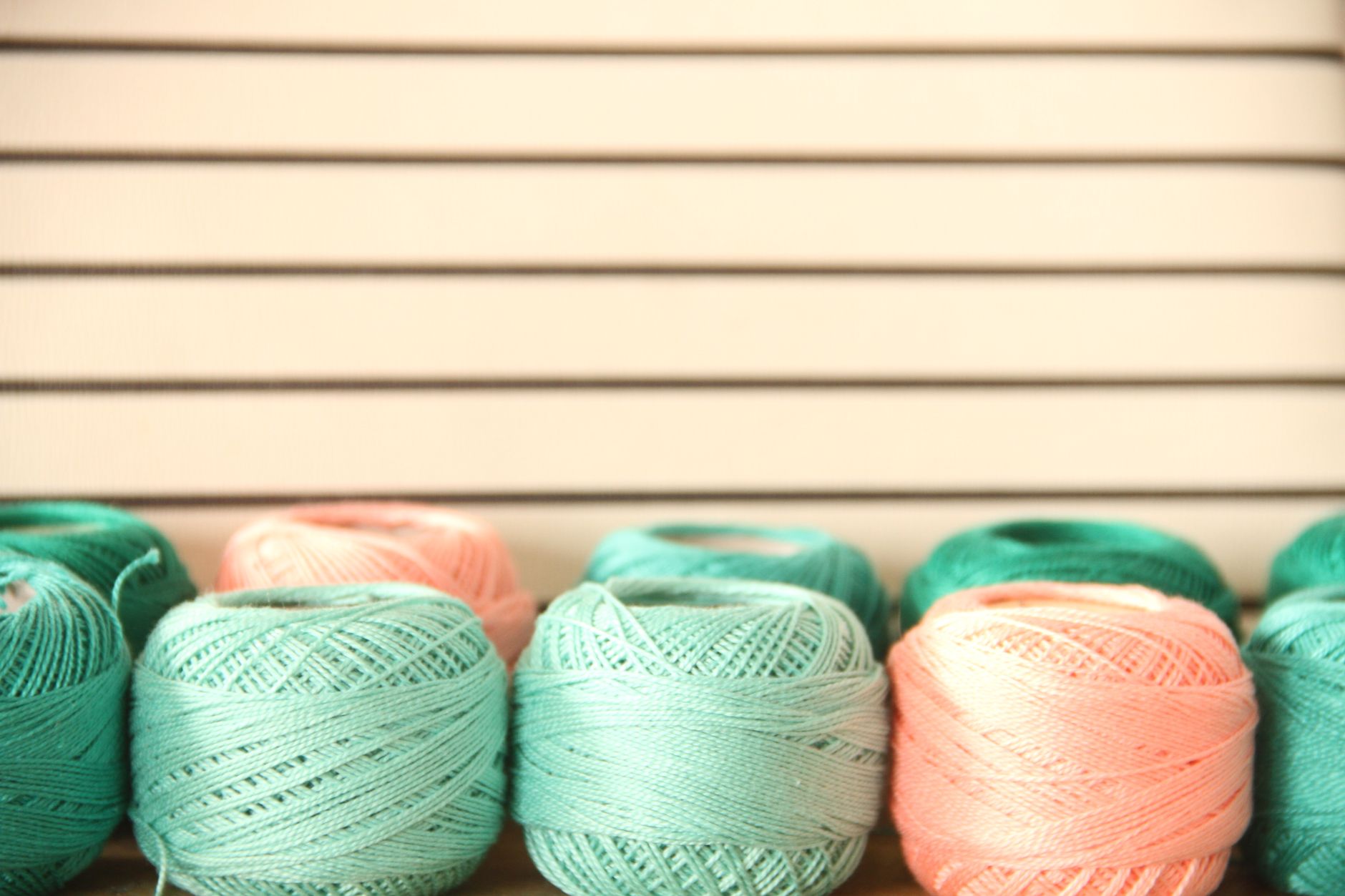 A collection of pastel yarn balls arranged in an orderly manner against a striped backdrop.