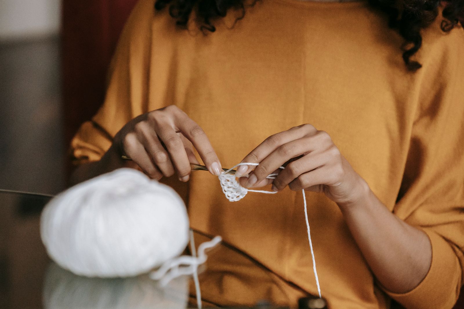 Close-up of a woman crocheting with white yarn, focusing on hands and craftwork.
