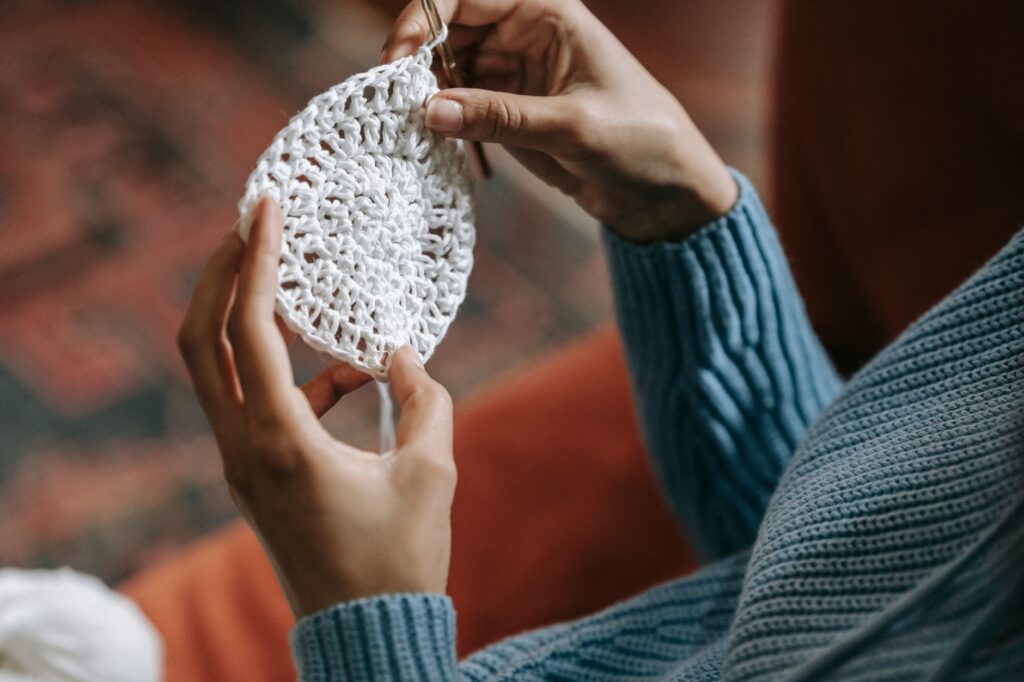 Close-up view of hands knitting a delicate white crochet pattern, highlighting the details and texture.
