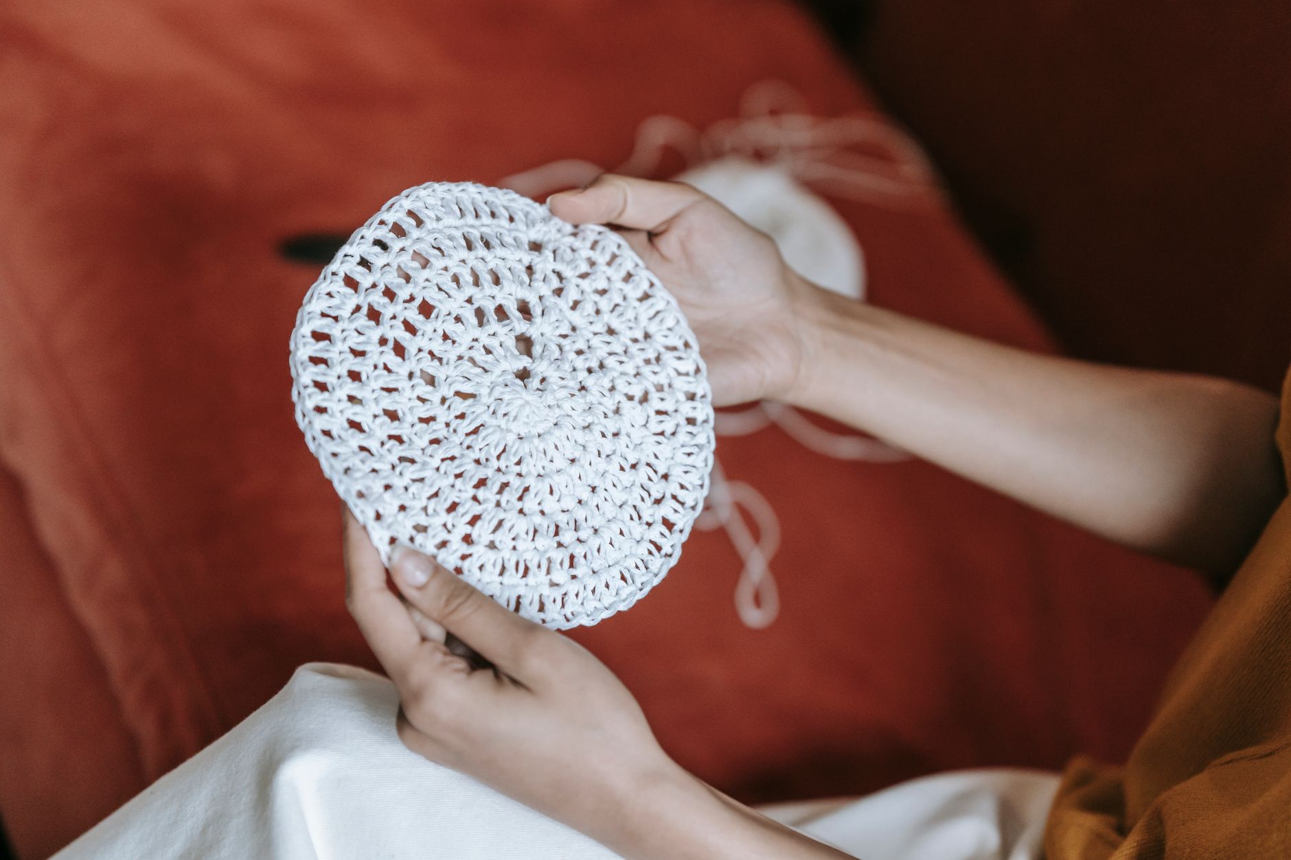 A detailed view of female hands holding a handmade crochet piece, indoors with warm tones.