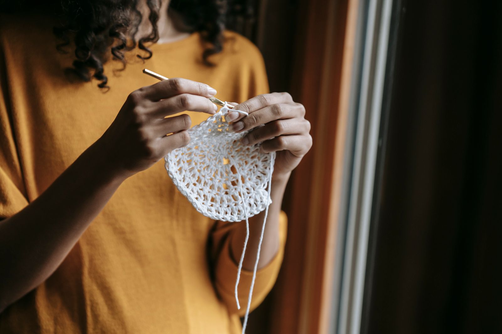 Crop anonymous female artisan with yarn and hook crocheting while having spare time in house