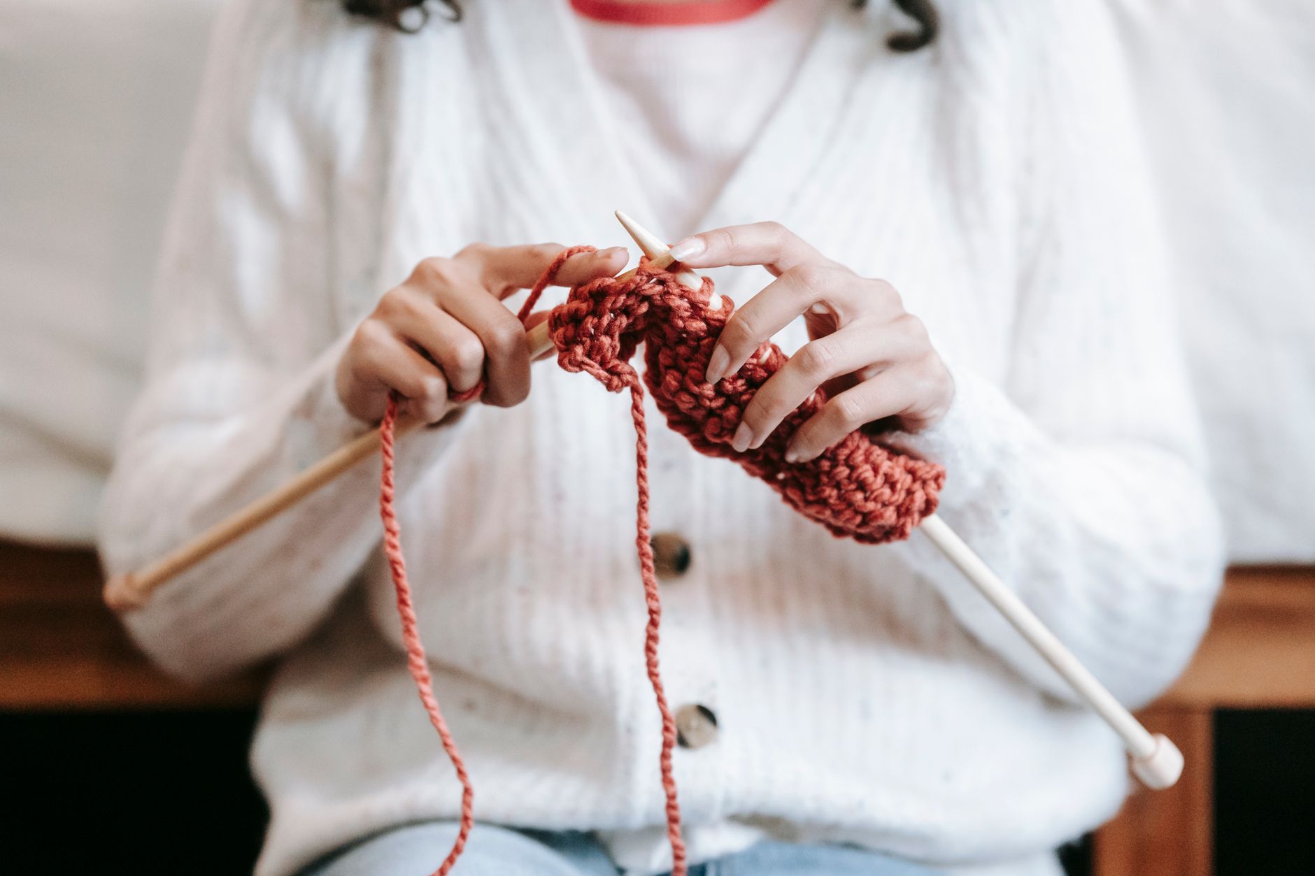 Crop unrecognizable female wearing warm woolen cardigan sitting on chair and knitting with needles and yarn