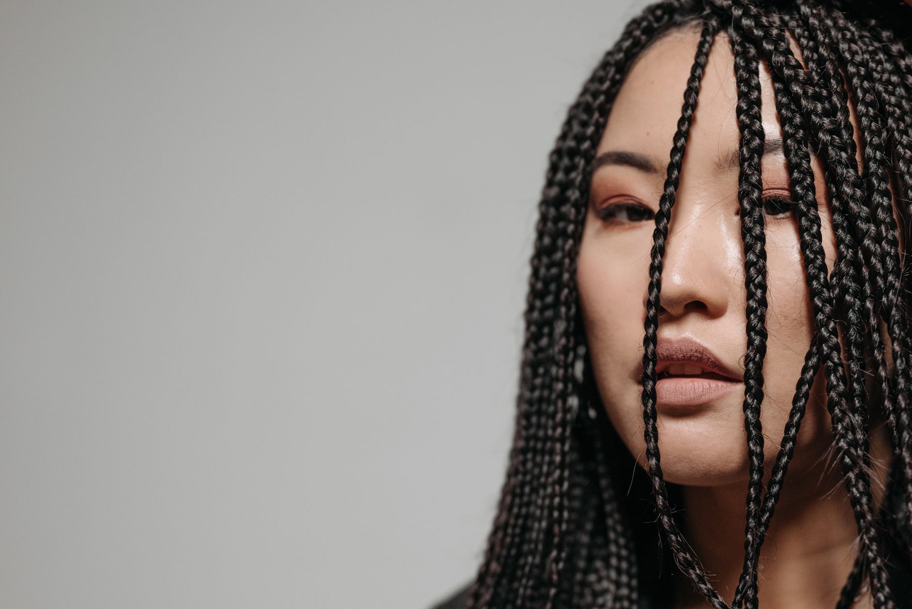Detailed close-up of an Asian woman with braided hair against a gray background.