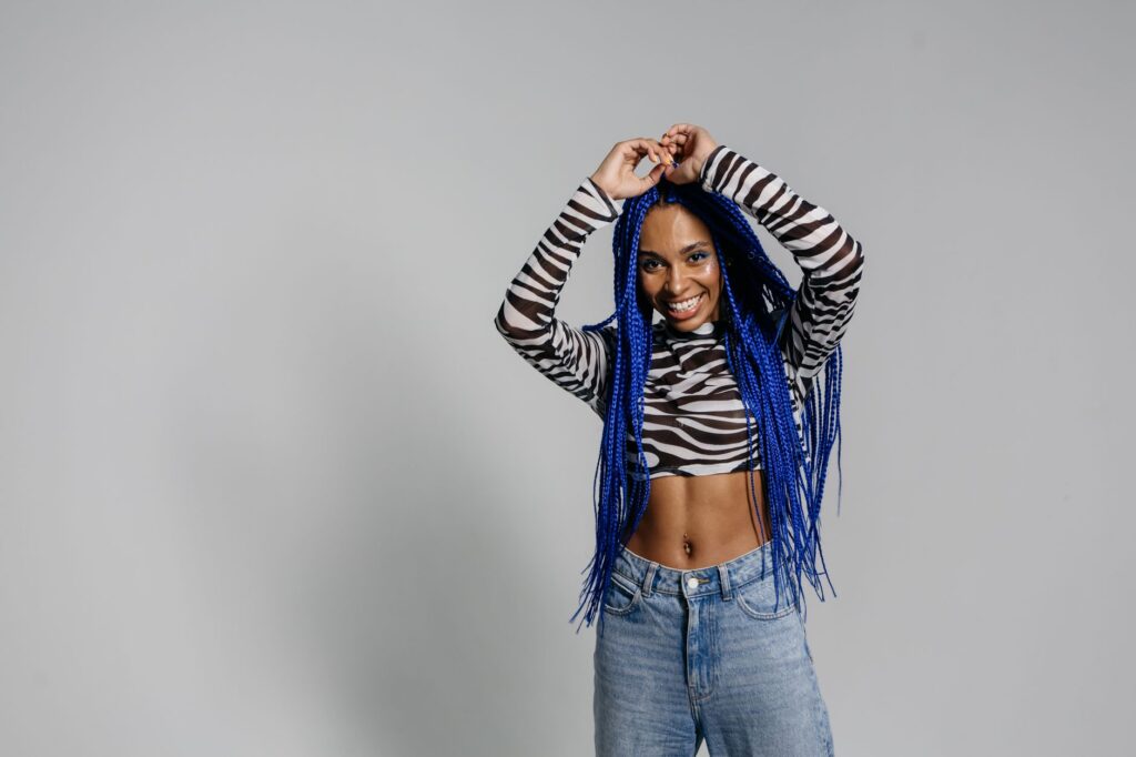 Smiling woman with blue braided hair, zebra top, and denim in studio setting.