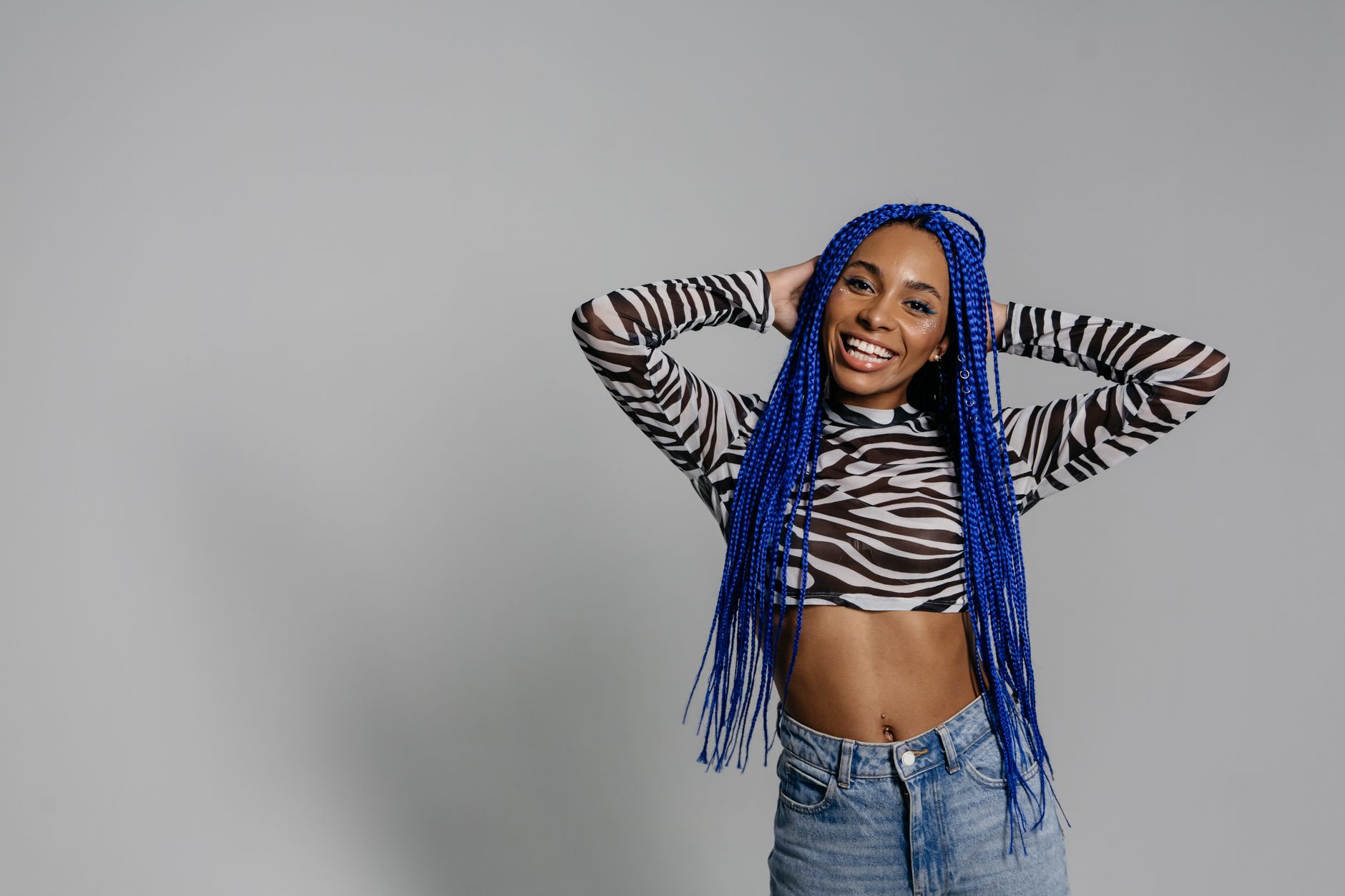 Confident woman with blue braids poses in zebra crop top, smiling.