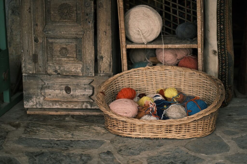 Colorful yarn balls in a wicker basket beside a rustic wooden cabinet, perfect for crafting inspiration.